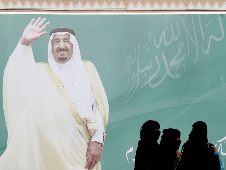 Women walk past a poster of Saudi Arabia&#39;s King Salman bin Abdulaziz Al Saud